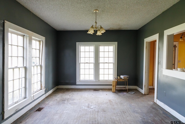 empty room with a textured ceiling, a chandelier, and plenty of natural light