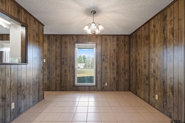 empty room with a notable chandelier, wood walls, and light tile patterned floors