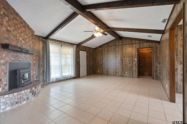 unfurnished living room featuring a wood stove, vaulted ceiling with beams, a textured ceiling, wooden walls, and light tile patterned floors