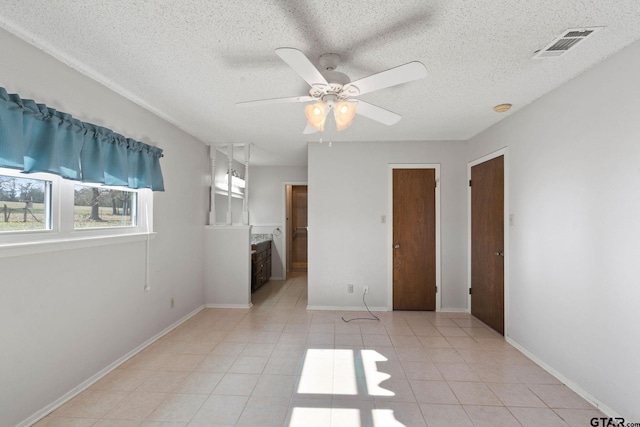 unfurnished bedroom featuring a textured ceiling, ceiling fan, a fireplace, connected bathroom, and light tile patterned flooring