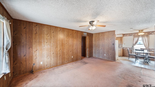 carpeted empty room featuring ceiling fan, wooden walls, and a textured ceiling