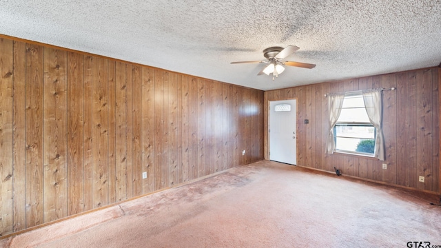 carpeted spare room with ceiling fan, a textured ceiling, and wood walls