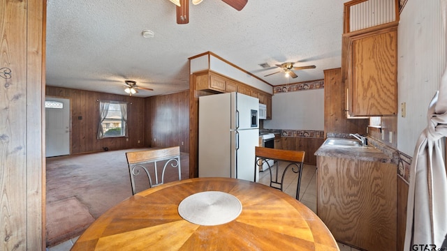 carpeted dining area featuring ceiling fan, a textured ceiling, and wood walls