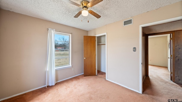 unfurnished bedroom featuring ceiling fan, a closet, light carpet, and a textured ceiling