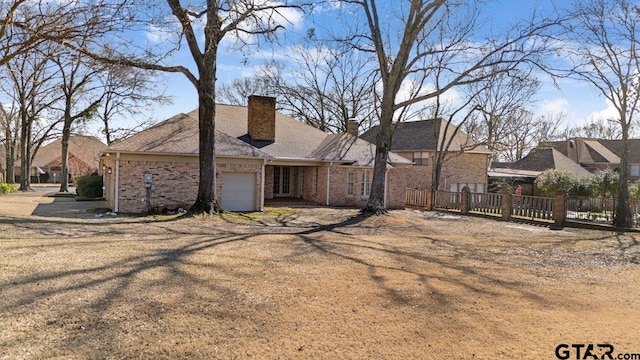 view of side of property featuring a garage, brick siding, a chimney, and fence