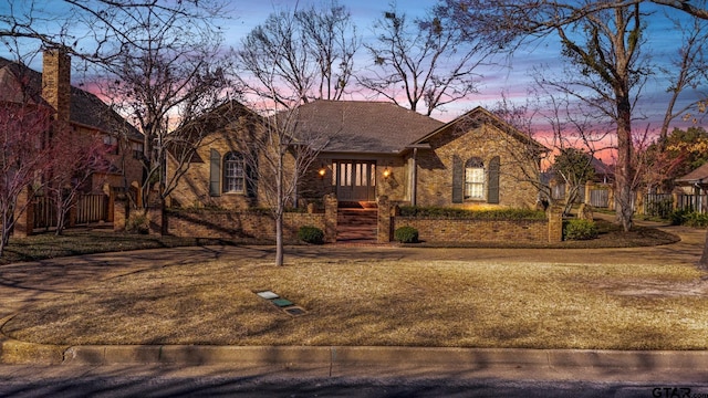 view of front facade featuring roof with shingles, fence, and brick siding