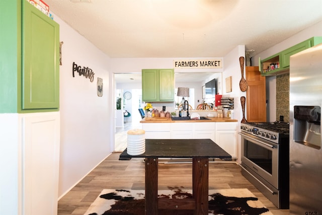 kitchen with a sink, light countertops, light wood finished floors, appliances with stainless steel finishes, and green cabinetry