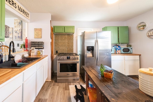 kitchen with green cabinetry, a sink, light wood-style floors, appliances with stainless steel finishes, and white cabinetry
