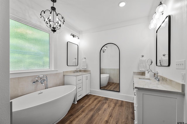 bathroom with a sink, an inviting chandelier, two vanities, wood finished floors, and a freestanding bath
