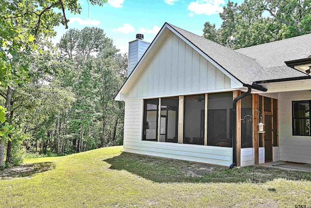back of house with a chimney, a yard, a sunroom, and roof with shingles