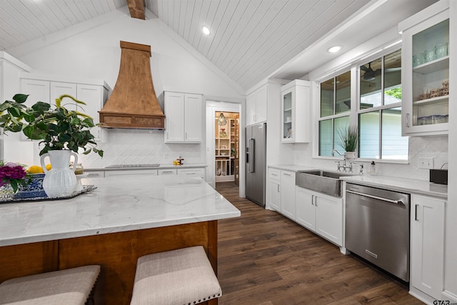 kitchen with a sink, stainless steel appliances, glass insert cabinets, light stone counters, and premium range hood