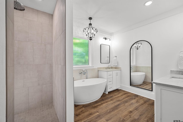 bathroom with an inviting chandelier, a freestanding tub, a tile shower, two vanities, and wood finished floors