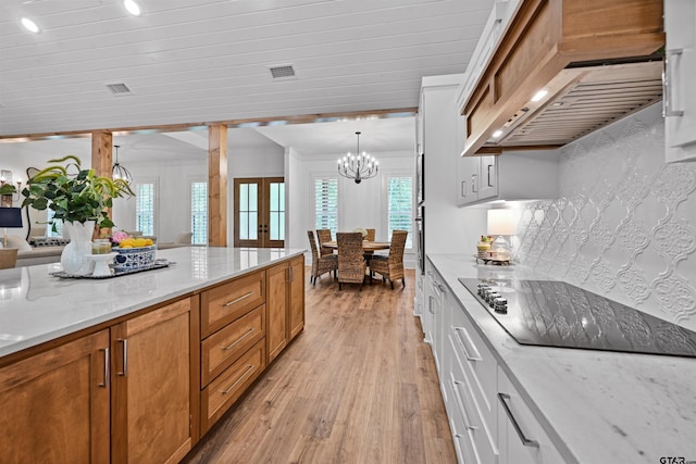 kitchen featuring visible vents, an inviting chandelier, black electric cooktop, light wood-type flooring, and premium range hood