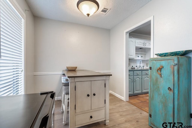 interior space featuring sink, light hardwood / wood-style flooring, tasteful backsplash, a textured ceiling, and kitchen peninsula