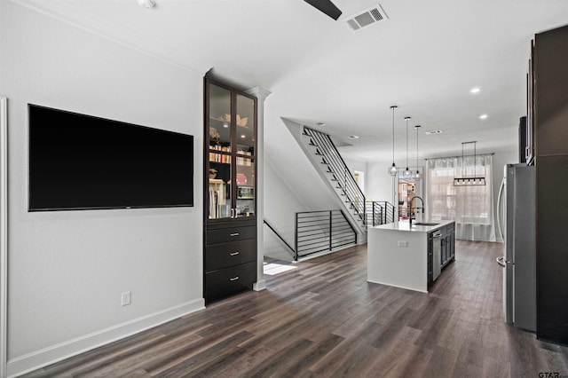 kitchen featuring hanging light fixtures, dark wood-type flooring, a center island with sink, and sink