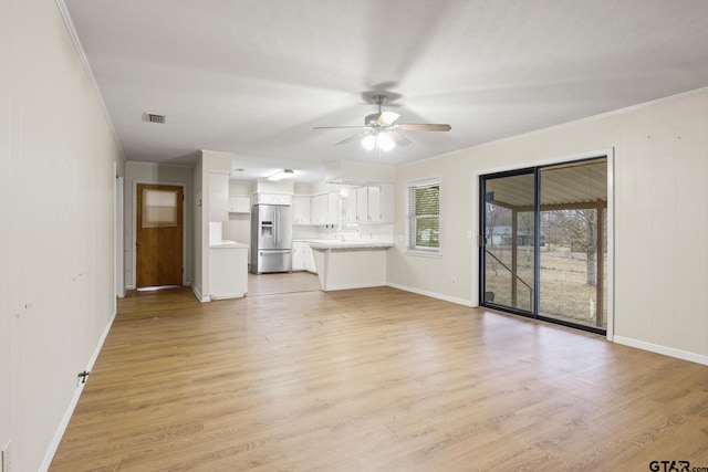 unfurnished living room with ceiling fan, ornamental molding, and light wood-type flooring