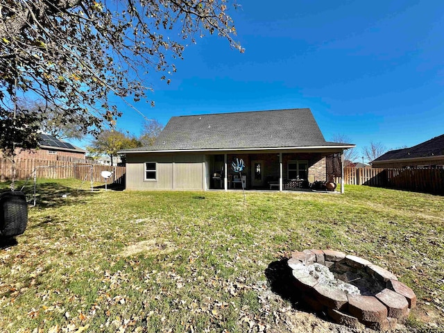 rear view of property featuring an outdoor fire pit and a lawn