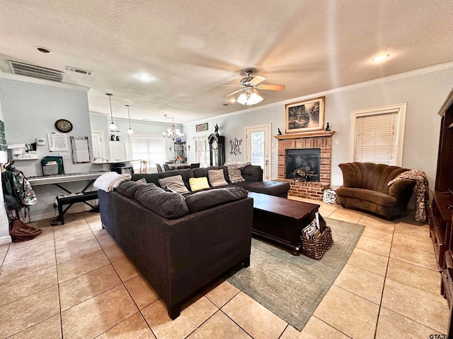 living room with a brick fireplace, ornamental molding, ceiling fan with notable chandelier, a textured ceiling, and light tile patterned flooring