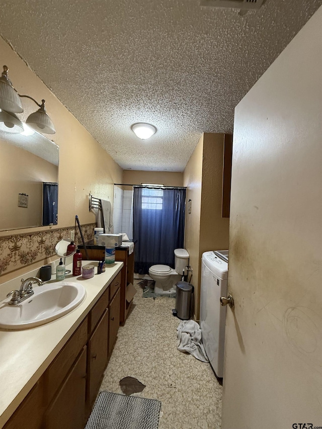 bathroom featuring a textured ceiling, toilet, washer / dryer, and vanity