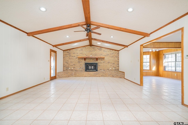 unfurnished living room featuring ceiling fan, vaulted ceiling with beams, wood walls, a fireplace, and light tile patterned flooring