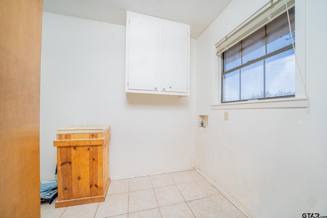 clothes washing area with washer hookup, cabinets, light tile patterned floors, and a textured ceiling