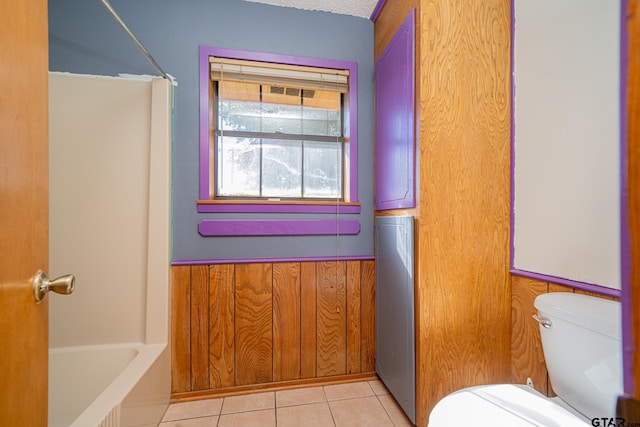 bathroom with tile patterned flooring, bathing tub / shower combination, a textured ceiling, toilet, and wooden walls