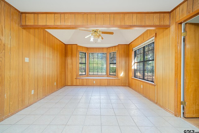 tiled empty room with ceiling fan and wood walls