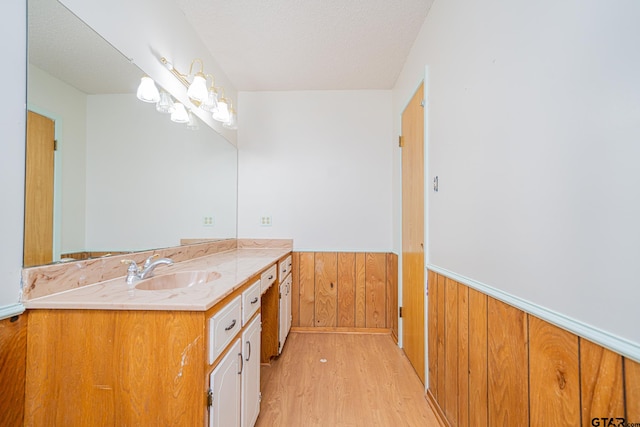 bathroom featuring hardwood / wood-style flooring, vanity, a textured ceiling, and wooden walls