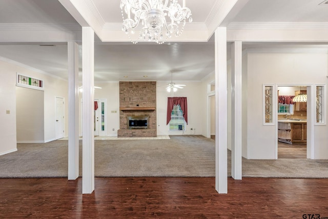 unfurnished living room featuring ceiling fan with notable chandelier, crown molding, a large fireplace, and dark hardwood / wood-style flooring