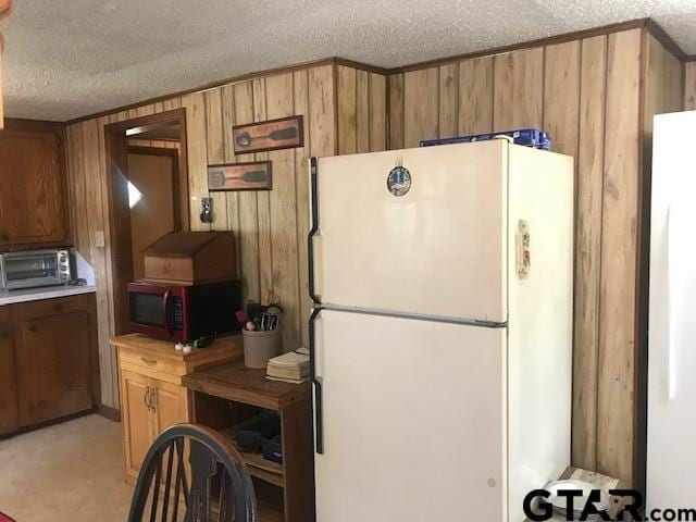 kitchen with a textured ceiling, white fridge, and wood walls