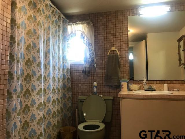 bathroom featuring walk in shower, vanity, tile walls, and toilet