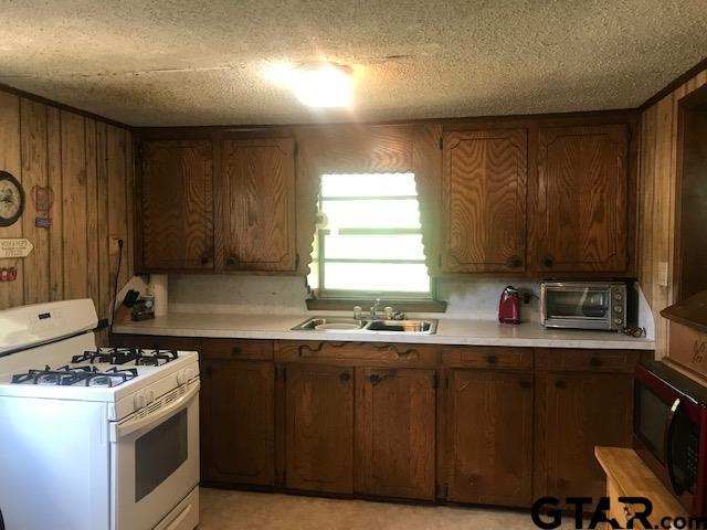 kitchen featuring white gas range, wooden walls, sink, and a textured ceiling