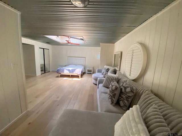 bedroom featuring light hardwood / wood-style floors, wooden walls, and a skylight