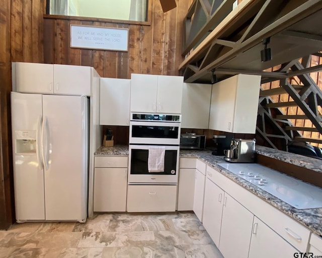 kitchen with white cabinets, multiple ovens, white fridge with ice dispenser, and wooden walls