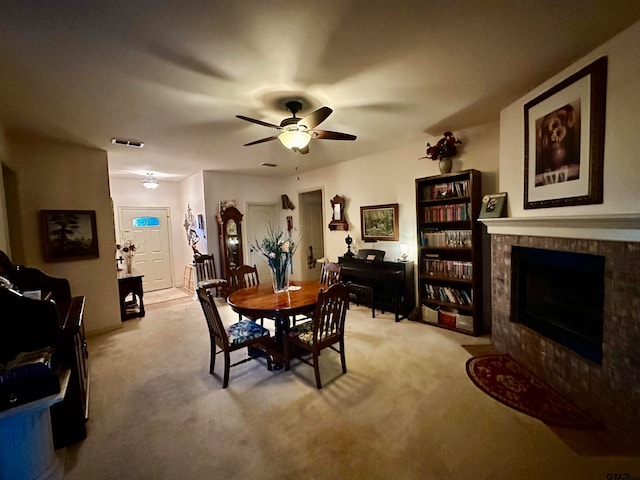 dining space featuring ceiling fan, a tile fireplace, and light carpet