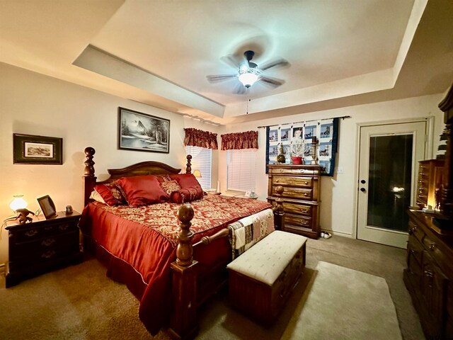 bedroom with dark colored carpet, ceiling fan, and a raised ceiling