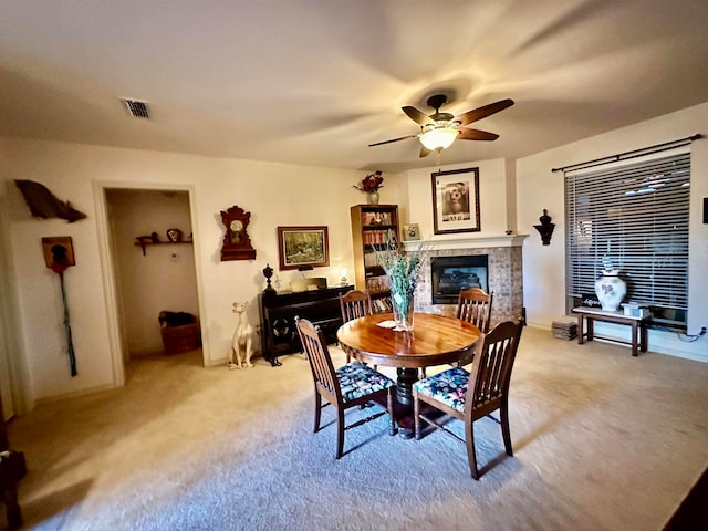 carpeted dining room with a fireplace and ceiling fan