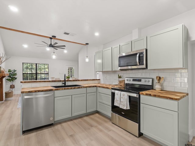 kitchen with stainless steel appliances, kitchen peninsula, hanging light fixtures, sink, and butcher block countertops