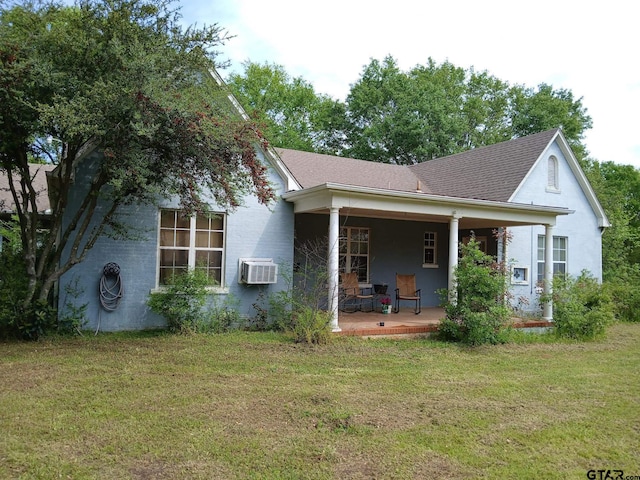 back of house with a yard, an AC wall unit, a shingled roof, and covered porch