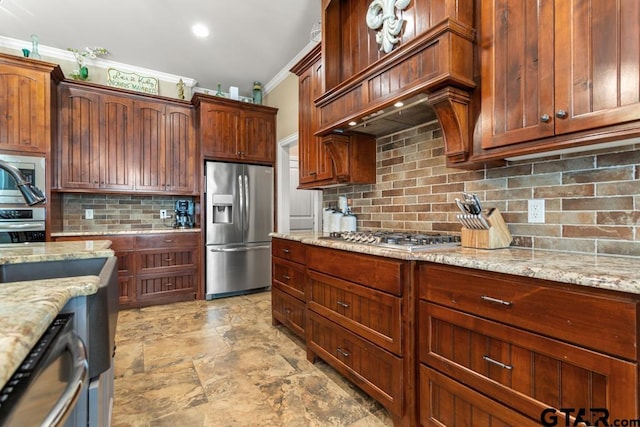 kitchen featuring light stone countertops, backsplash, premium range hood, ornamental molding, and stainless steel appliances