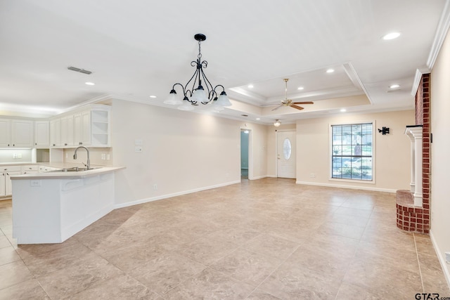 unfurnished living room featuring ceiling fan with notable chandelier, a raised ceiling, crown molding, and sink