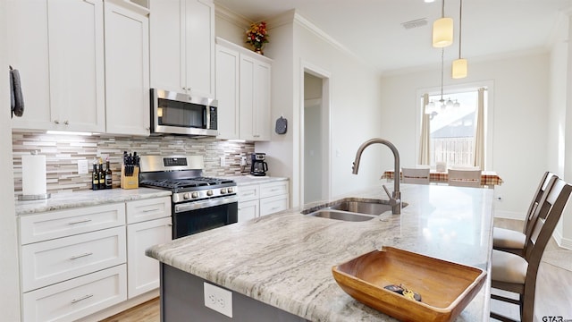 kitchen with pendant lighting, appliances with stainless steel finishes, sink, white cabinets, and a center island with sink