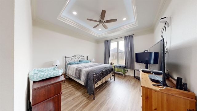 bedroom with ornamental molding, ceiling fan, light hardwood / wood-style flooring, and a tray ceiling