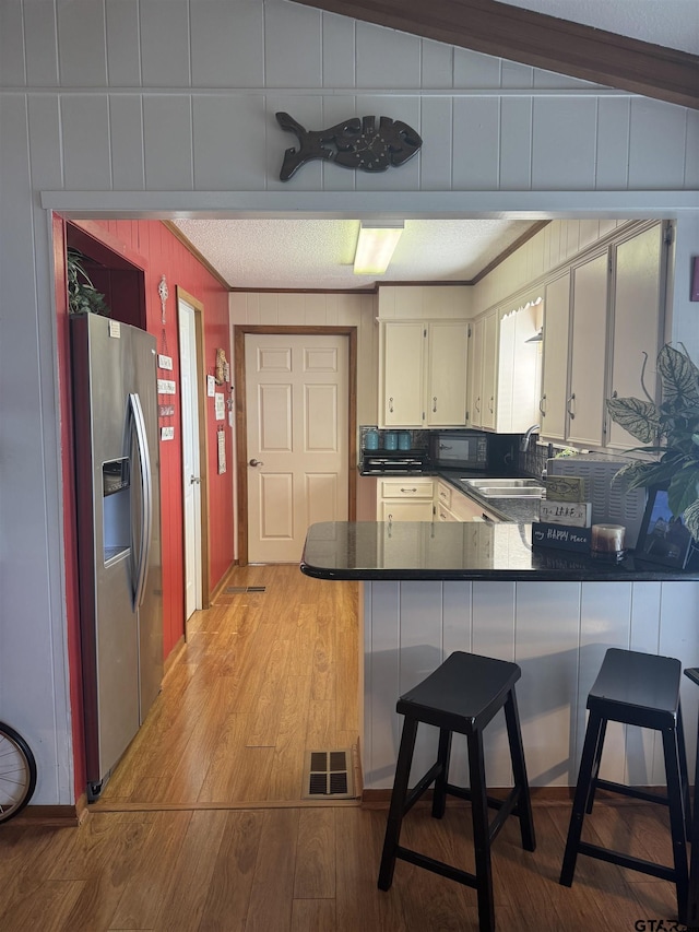 kitchen featuring sink, light hardwood / wood-style flooring, a kitchen breakfast bar, stainless steel refrigerator with ice dispenser, and kitchen peninsula