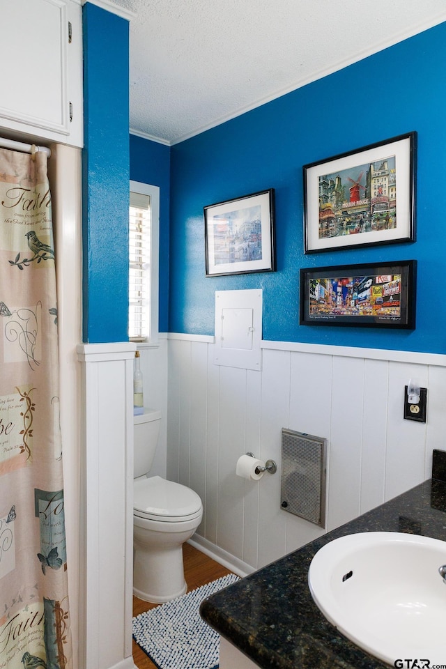 full bath with a wainscoted wall, toilet, a textured ceiling, wood finished floors, and vanity