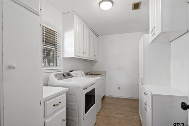 washroom featuring visible vents, cabinet space, light wood-style floors, and washing machine and clothes dryer