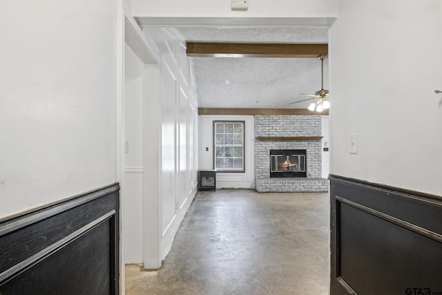 unfurnished living room featuring a textured ceiling, ceiling fan, concrete flooring, wainscoting, and a brick fireplace