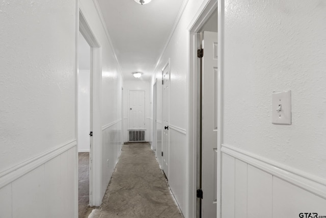 hall featuring crown molding, concrete flooring, wainscoting, and a textured wall