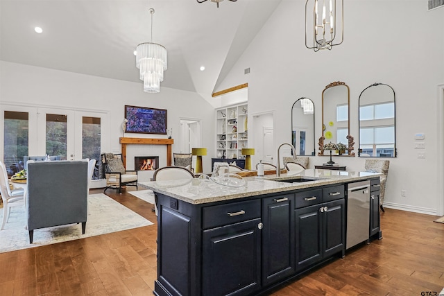 kitchen with sink, stainless steel dishwasher, light stone countertops, an island with sink, and decorative light fixtures