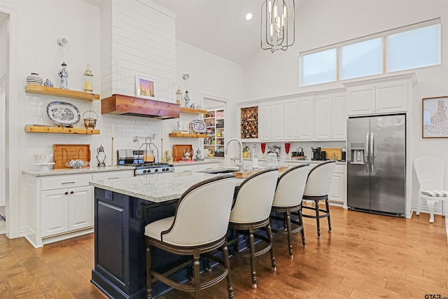 kitchen featuring a breakfast bar, high vaulted ceiling, hanging light fixtures, an island with sink, and stainless steel appliances